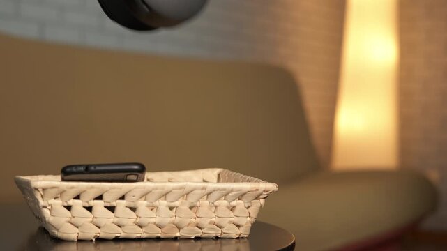 Woman relaxing at home after digital detox. Woman places a smartphone and headphones in a basket on a table before sits on the sofa in the background, embracing tranquility