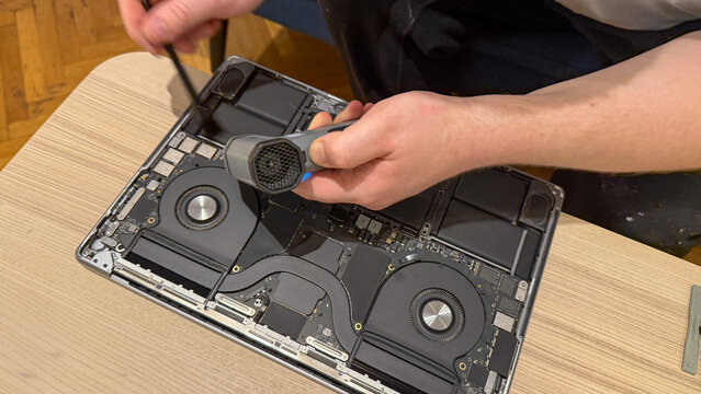 A Caucasian male engages in meticulous laptop cleaning, integrating tech zen with National Clean Your Desk Day and DIY ethos