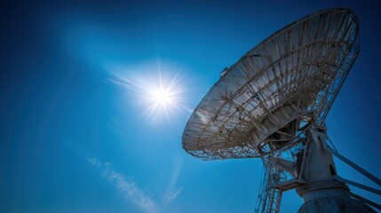 Large parabolic satellite dish antenna pointed skyward against a clear blue sky with a bright sun
