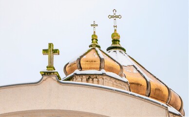 Golden domes topped with crosses gleam against a light sky, partially covered with snow. The architecture features ornate details and curves. © Ron