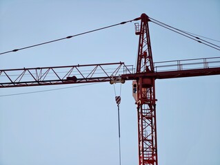Red crane cables with tensioned hardware details. Close view of crane jib with pulley system against sky