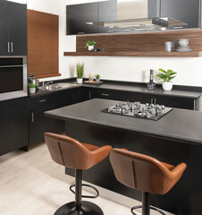 a modern kitchen with black and gray counters and brown chairs in it, close up view