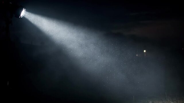 Focused projection light beam piercing misty night air creating a glowing shaft of light amid softly diffused surroundings.