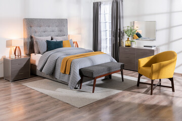 A modern bedroom featuring a large bed, a yellow chair, a dresser, and a wooden bench, a cozy interior space © Jesus