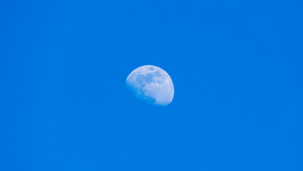 Detailed daytime partial moon against bright blue cloudless sky