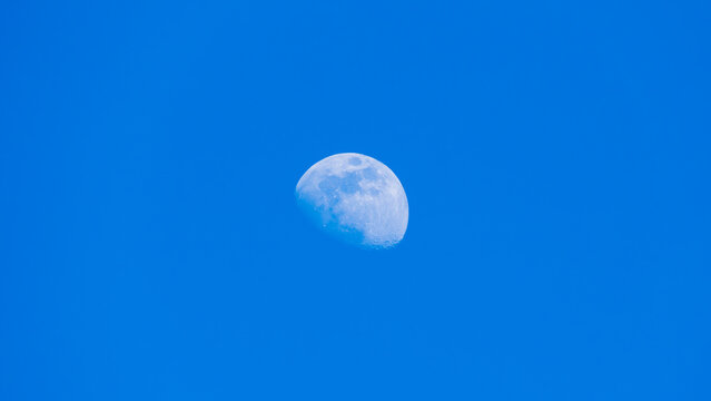 Detailed daytime partial moon against bright blue cloudless sky