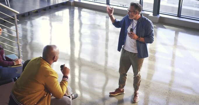 Mature man responding to question from African American man raising mic and gesturing in atrium