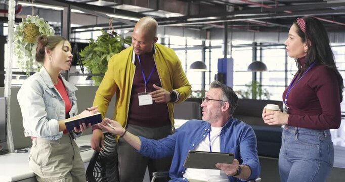 Diverse coworkers in office showing tablet, writing notes, nodding, raising cup, reaching consensus
