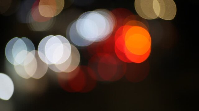 The film captures an artistic, out-of-focus view of city traffic at night. Blurred headlights and taillights transform into glowing orbs of red, white, and yellow, creating a dreamy bokeh effect. The 