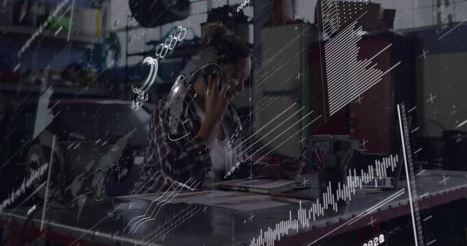 Woman taking phone call, making notes and consulting laptop in workshop, HUD charts guiding repairs