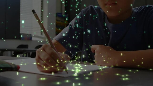 Boy writing with pencil on paper at class desk camera rising green particles drifting for classwork
