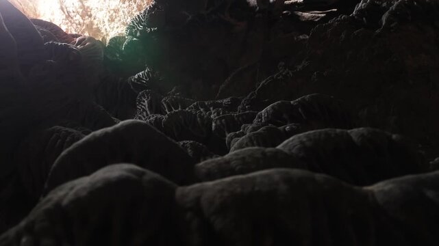 Panning view inside Ibiza limestone cave over textured rock formations leading toward bright natural opening illuminated by Mediterranean sunlight.