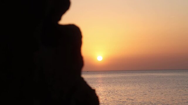 Golden sunset over the Mediterranean Sea in Ibiza gradually revealed from behind a dark rock silhouette as the camera shifts sideways.
