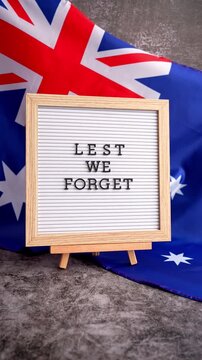 Somber Australian flag backdrop with text LEST WE FORGET on letter board. Respectful message for memorial ANZAC campaigns. Concept of remembrance and honor