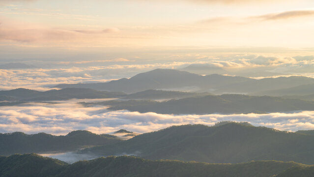 Low lying clouds drift between rolling Appalachian mountain ridges at golden sunrise, creating layers of misty peaks and valleys in soft morning light with peaceful, serene atmosphere