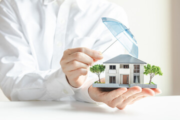 傘で安全に守られる家の模型　住宅の火災保険や地震保険　家のセキュリティ