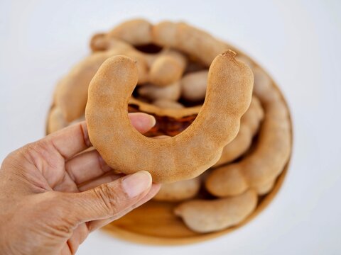 Several sweet tamarind pods are arranged on a wooden tray placed on a white surface. This is a delicious, sweet Thai fruit from Phetchabun province.