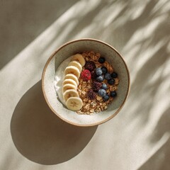 Fototapeta premium Healthy breakfast bowl with oatmeal, yogurt, banana slices, blueberries, and raspberries under harsh natural sunlight