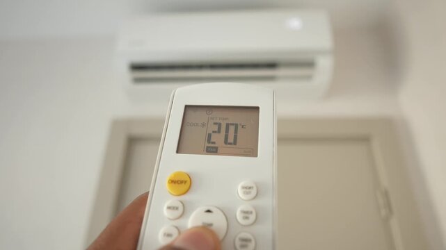 Person lowering air conditioner temperature with remote control at home for better indoor climate