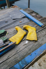 Fototapeta premium Pair of Dirty Yellow Rubber Safety Boots on Rustic Wooden Pier