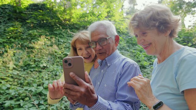 Three White Seniors Exploring App Outdoors, Smartphone Navigation On Leafy Trail, Smiles And Curiosity, Casual Shirts And Glasses, Sunlit Forest Backdrop, Active Mature Friends Sharing Discovery