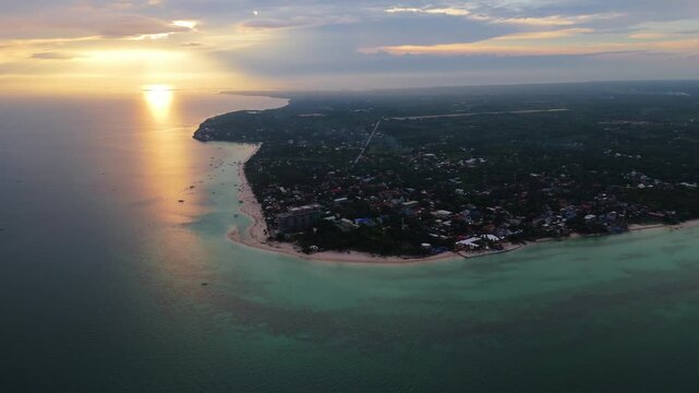 A breathtaking aerial drone shot of Bantayan Island at sunset, showing the golden sun reflecting on the calm sea and the tropical coastline of the Philippines
