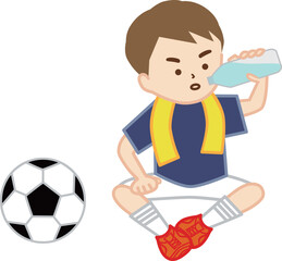 首にタオルを巻いて地面に座って水分補給をするサッカー少年
