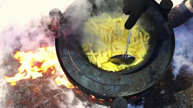 Outdoor cooking scene with visible steam and glowing embers. Rustic lifestyle concept and wilderness food preparation. Top view of hot pan with potato and beef meat.