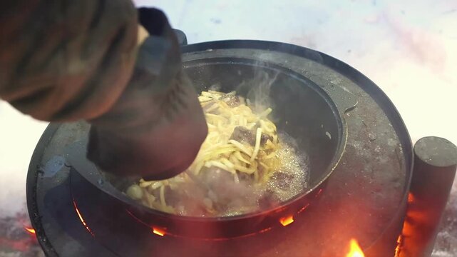 Close up of gloved hand preparing hot food outdoors in winter. Adventure travel concept, warmth and traditional cooking experience. Rice with beef steaming.
