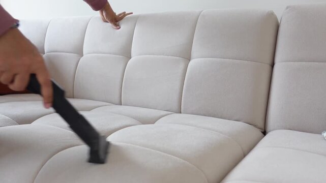 Woman cleaning white couch using vacuum cleaner with nozzle attachment in bright living room