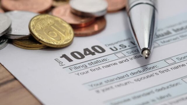 Close-up cinematic motion footage of tax form 1040 with pen and coins on table for financial planning and annual income tax declaration deadline concept