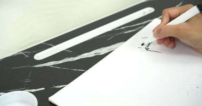 a woman is writing the Arabic sentence Basmalah or Bismillahirrahmanirrahim which has the meaning of saying the name of Allah, the Most Gracious and Most Merciful, using a black marker on white paper