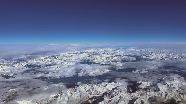 Hyperlapse x5 of an aerial view of The snow covered Alps mountains with some low clouds over the mountains under a blue sky. Simulated supersonic flight experience. 4K shot. 8000m high.