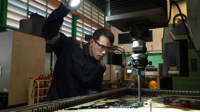 Asian male engineer foreman, in charge of operating automatic machinery, is currently watching and using tools to inspect the quality of metal cutting machines and automotive parts in a car parts manu
