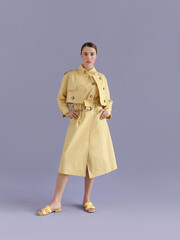 Young beautiful woman with brown hair wearing trendy clothes yellow trench coat and sndals looking confident fresh and lovely Fashion model full length body studio portrait on purple background  © Tatiana