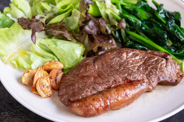 Juicy steak with garlic and leafy salad, sauteed greens and mixed lettuce on plate, appetizing home meal