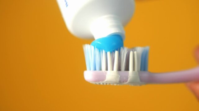Blue toothpaste gel being squeezed onto toothbrush head against yellow background