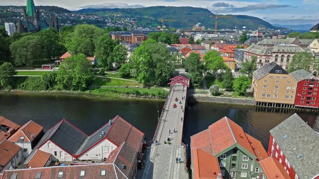 Aerial drone view of Gamle Bybro bridge over Nidelva River in Trondheim, Norway. Norwegian riverside warehouses and colorful historic buildings frame the span.