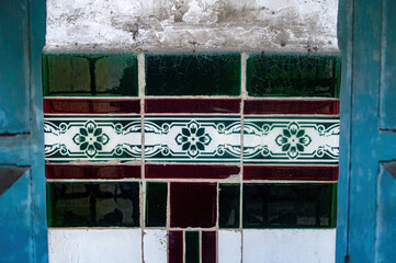 Obraz premium An aged wall column features vibrant green and maroon patterned tiles, framed by a peeling, distressed wall and blue elements, blending decay with color