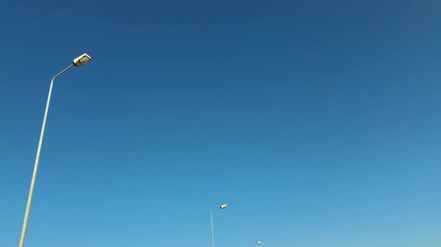 Upward motion view of street pillar lamps over road against blue sky