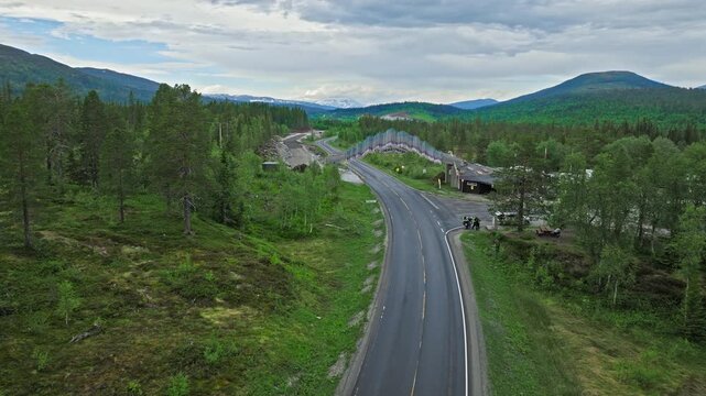 Aerial drone view of Tr&oslash;ndelag boundary bridge over a road in Norway. Norwegian Tr&oslash;ndelag sign spans the arch above passing traffic and pine forest.