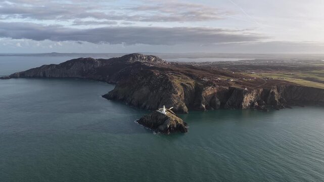 Aerial drone footage of South Stack Lighthouse on the rugged Welsh coast, dramatic cliffs and Atlantic waves, cinematic seascape ideal for travel, nature, coastal tourism and documentary use.