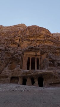 Handheld vertical pan across rock-cut facade at Little Petra (Siq al-Barid) near Petra, Jordan. Ancient Nabatean architecture carved into sandstone cliff