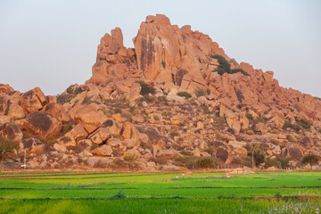 Iconic rocky landscape of Hampi with granite boulder formations and green rice fields at sunrise, Karnataka, India. © Schilo