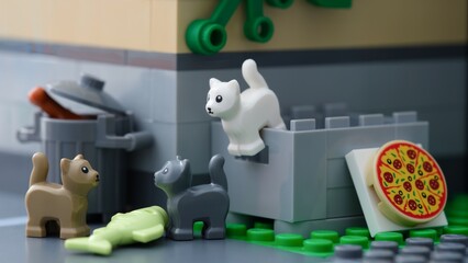 Fototapeta premium Tambov, Russian Federation - July 02, 2025 Lego cats standing behind a building near a crate and trash can with a pizza and fish