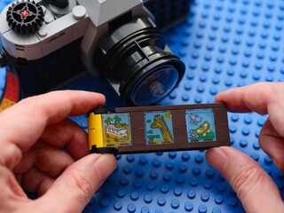 Fototapeta premium Tambov, Russian Federation - February 20, 2026 Person hands holding a toy film strip from the LEGO Creator 3in1 Retro Camera building set with a vintage-style brick-built camera in the background.