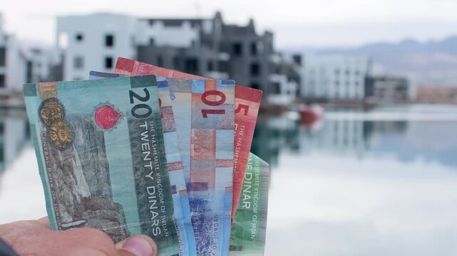 Jordanian dinar banknotes in hand, economy finance cash concept, real estate investment background. Ayla. Holidays in Jordan, red sea vacation, property purchase, israel border zone concept