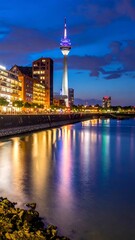 Obraz premium City skyline with a tall tower lit against a dusk sky reflected in water