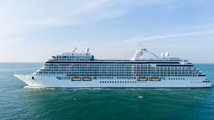 Massive luxury cruise ship sailing across the deep blue ocean water under a clear sunny sky. Summer vacation, tropical travel destination, and global tourism industry business concept.
