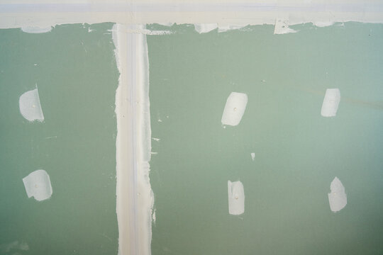 Green gypsum board wall with white joint compound spots covering screw holes. Drywall installation process in a construction site, preparing surface for painting and home interior renovation.
